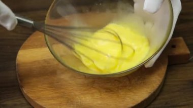 Person preparing homemade omelette mixing with whisk eggs. Close up.
