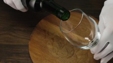 Skilled sommelier pouring red wine from bottle into Glass. Close up.