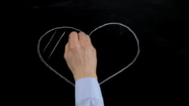 Male hand draws heart symbol in chalk on a blackboard. Close up.