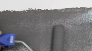Roller painting the wall, gray paint over white. Close up.