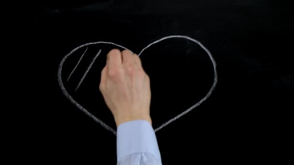 Male hand draws heart symbol in chalk on a blackboard. Close up. — ストック動画