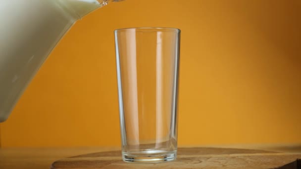 Cerrar Leche vertida en vidrio del frasco sobre tabla de madera con fondo de color. De cerca. . — Vídeos de Stock