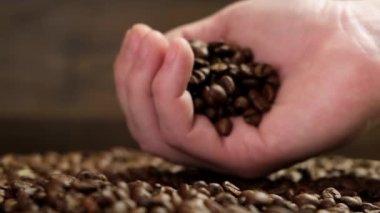 Male hand spills coffee beans on table. Close up.
