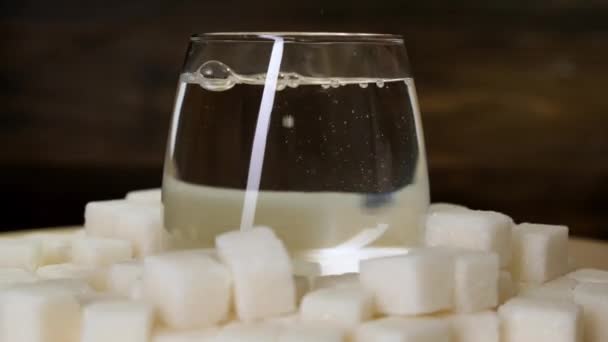 Sugar pieces and glass of water rotates on black background. Close up. — Stock Video