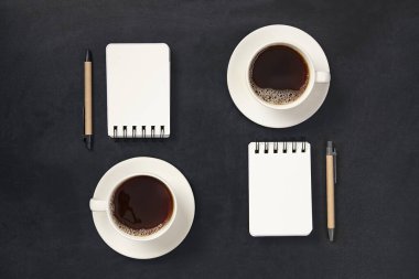 Siyah arka planda siyah kalemli, defterli bir fincan kahve. İş planlayıcısı.