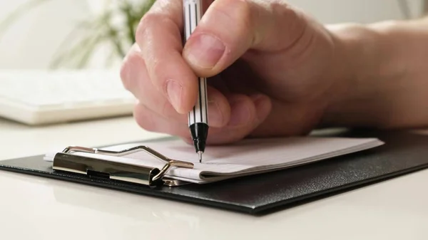 Handen låg på bordet, höll i en penna och skrev. Närbild. — Stockfoto