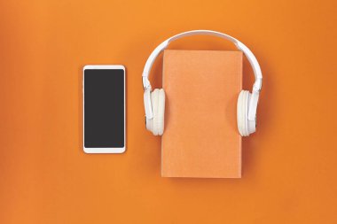 Kitaplı kulaklıklar ve turuncu arka planda akıllı telefon..