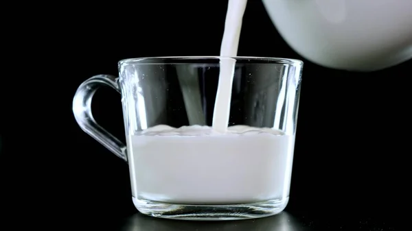 Versare il latte in una tazza trasparente su fondo nero. Da vicino. . — Foto Stock