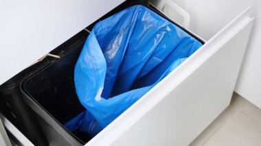 Blue Garbage bag replacement in small kitchen trash. Close up. clipart