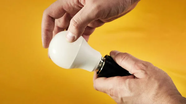 Mężczyzna ręce skręcanie elektryczne oszczędzania żarówki na białym stole. Zamknij się.. — Zdjęcie stockowe