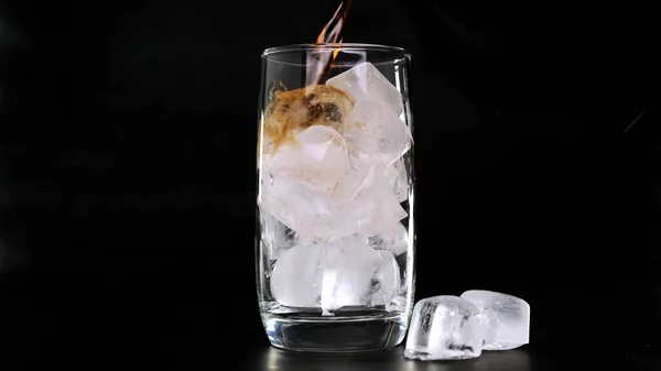 Cola mit Eiswürfeln in Glas auf schwarzem Hintergrund gießen. Nahaufnahme. — Stockfoto