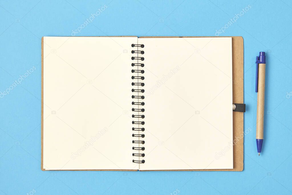 Open white paper with pen on a blue background. Top view.