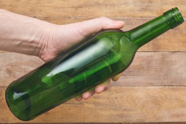 Ahşap arka planda şarap şişesini tutan bir el. Üst görünüm.