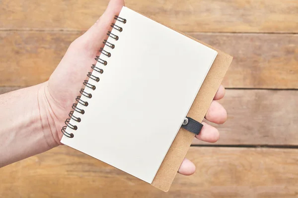 Hand mit Notizbuch-Rohpapier über Holztisch. Ansicht von oben. — Stockfoto