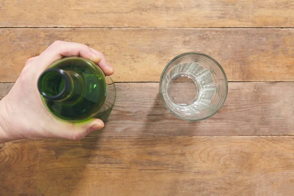 Houdt de fles vast op een houten tafel met glas. Bovenaanzicht. — Stockfoto