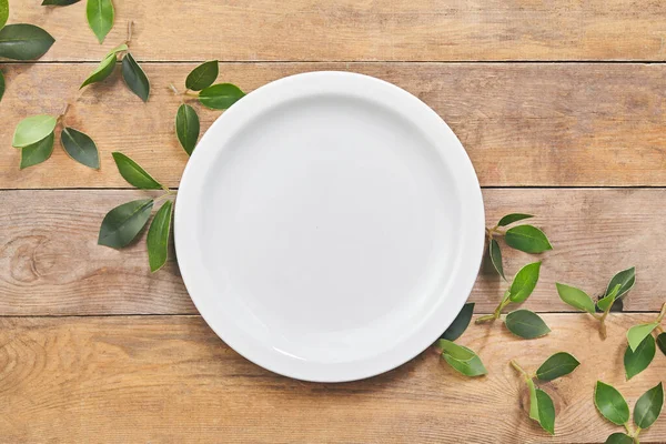 Leerer weißer Teller mit grünem Blatt auf Holztisch. Ansicht von oben. — Stockfoto