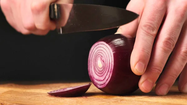 Hands cut red onions in kitchen on wooden board. Close up. — Stockfoto