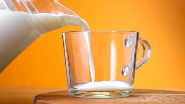 Milch in Glas gegossen aus Glas auf Holzplatte mit farbigem Hintergrund. — Stockfoto