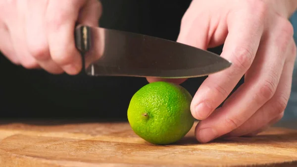 Trancher la lime fraîche en deux avec un couteau sur une planche à découper en bois. Gros plan . — Photo
