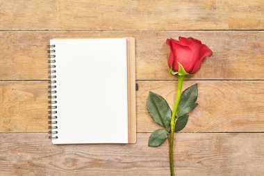 Boş defterin üst görüntüsü ve kırsal kahverengi ahşap masada kırmızı gül..