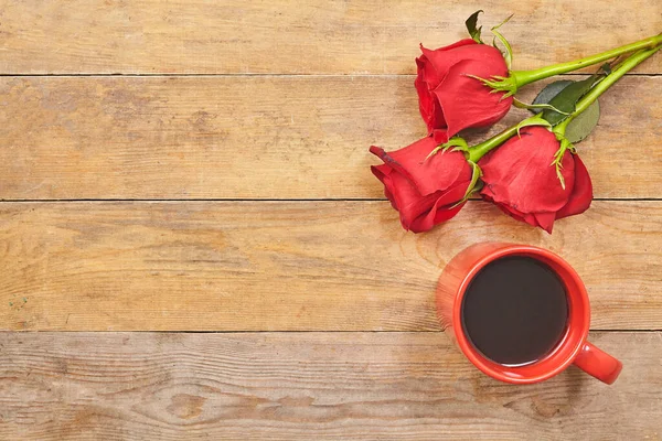 Rote Rosen und Tasse Kaffee auf hölzernem Hintergrund mit Kopierraum. Ansicht von oben — Stockfoto