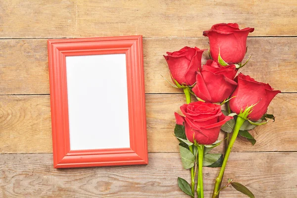 Red rose and blank photo frame on old wooden background. Top view. Royalty Free Stock Images