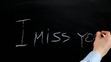 Hand writing i miss you with white chalk on blackboard. Close up.