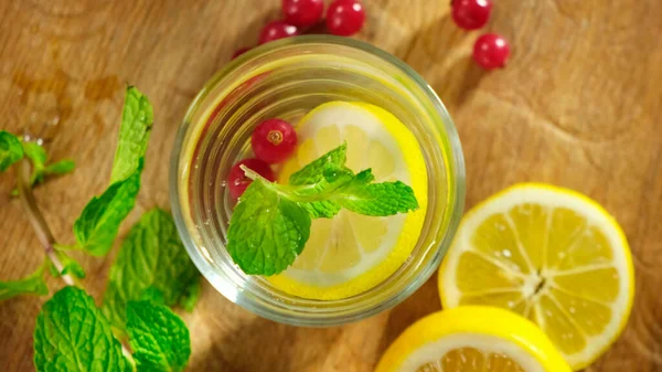 Glas mit kaltem Wasser, mit Zitrone, Beere, Eis und Minze rotierend. Nahaufnahme. — Stockfoto