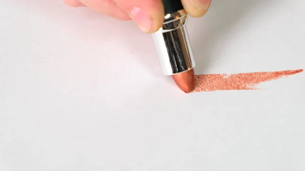 Female hand drawing line with brown lipstick on white surface. Close up. — Stock Photo, Image