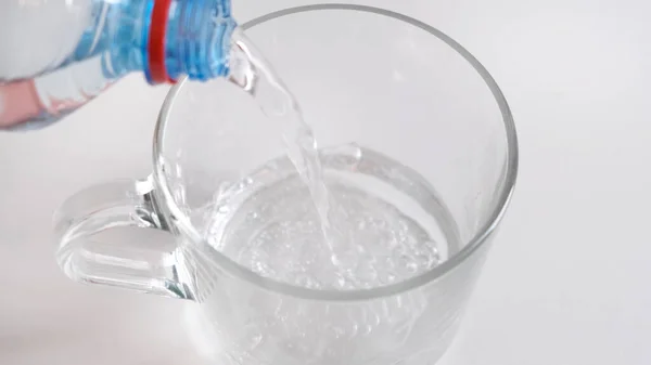 Pour a transparent glass water from bottle on white background. Close up. — Stock Photo, Image