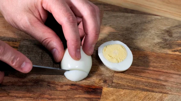 Uomo mani taglio uovo sodo su tavola di legno con coltello . — Foto Stock