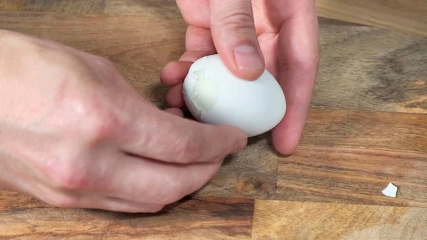 Manos masculinas limpia un huevo de gallina hervido a bordo . — Foto de Stock