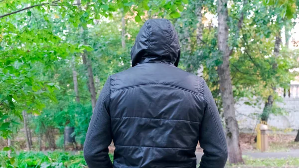 Homem de volta vestindo em um capuz preto. Caminhando pelo parque à noite . — Fotografia de Stock