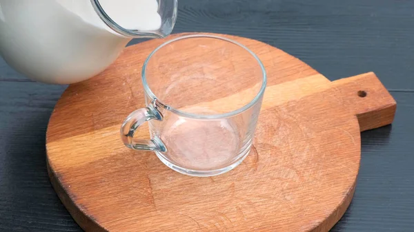 Close-up van het gieten van melk in glazen beker op een houten achtergrond. Houten ondergrond. — Stockfoto