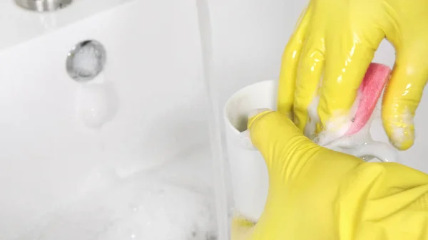 Persona en guantes de goma amarilla lavadora una taza en el fregadero de la cocina — Foto de Stock