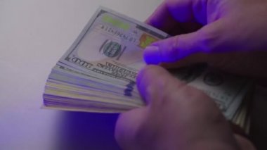 Adam parayı sayıyor. Beyaz bir masada 100 dolarlık banknotları saymak. Kapat.