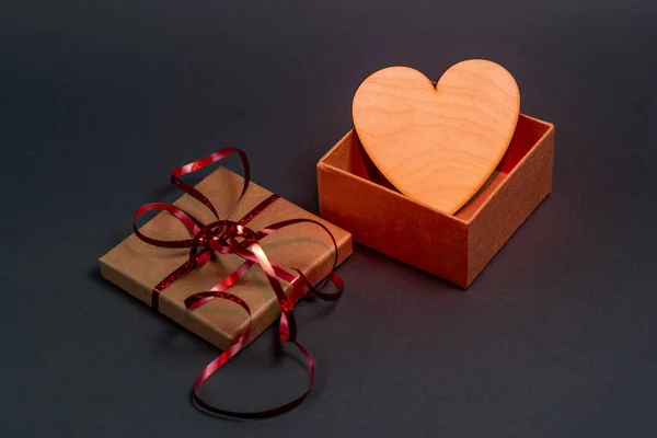 Caja de regalo con cinta roja y corazón de madera sobre fondo gris. Retroiluminación roja — Foto de Stock