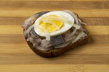 Sandwich with herring, onions and chicken egg on a wooden tray. National Russian cuisine