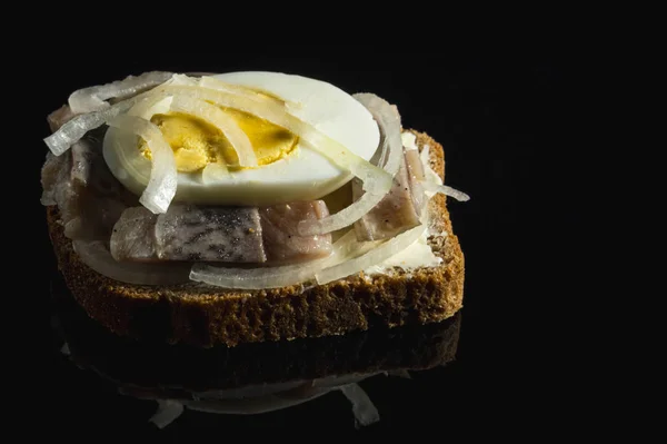 Sandwich with herring, onions and chicken egg. National Russian cuisine. Black glass background, close up — Stock Photo, Image