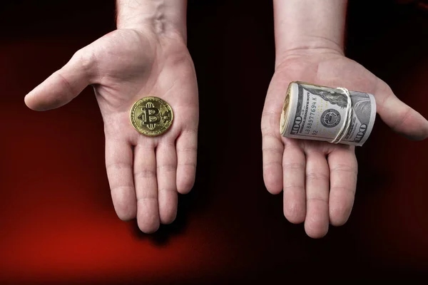 Біткоїн монета і пакет стодоларових банкнот у простягнутих руках. Концепція вибору — стокове фото