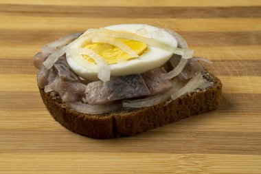 Sandwich with herring, onions and chicken egg on a wooden tray. National Russian cuisine