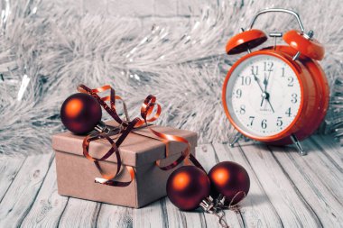 Hediye kutusu ve arka planda bulanık çalar saat. Yeni yıl ya da XMAS için süslenmiş ahşap bir masa ve kırmızı Noel toplarıyla süslenmiş. Boşluğu kopyala