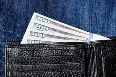 İçinde banknotlar ve kot pantolon olan siyah, hakiki deri bir cüzdan. Yumuşak odak