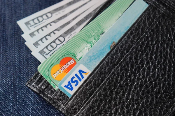 Odessa, Ukraine - April 12, 2020: Black genuine leather wallet with banknotes and credit card inside, jeans background. Soft focus — Stock Photo, Image