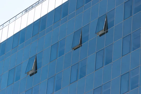 Glass transparent windows on the facade of a modern high-rise office or commercial building in the center of a big city reflect the blue sky