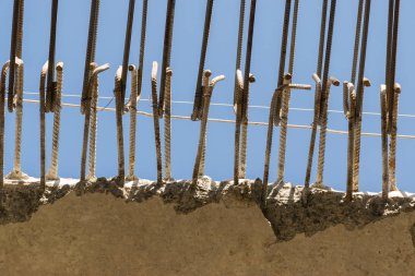 Mavi gökyüzüne karşı beton bloklardan çelik takviye çubukları.