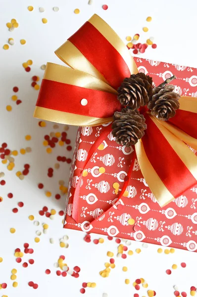 Beautiful red box for new year and Christmas gift. Gift in a red box with a pattern of white balls. Red box on white background. Preparation for the holiday. Merry Christmas and happy New year gift. Box decorated with a bow and fir cones