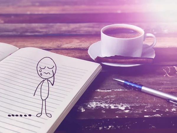 Crying man doodle in notepad with coffee and pen on wooden table