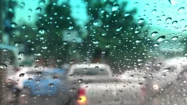 Araba ön camındaki yağmur damlasının odaklanmış görüntüsü, şehirdeki trafiği bulanıklaştırması, yağmur fırtınasında araba sürmesi, sokak lambasının renkli bokeh 'i, seçici odak noktası.