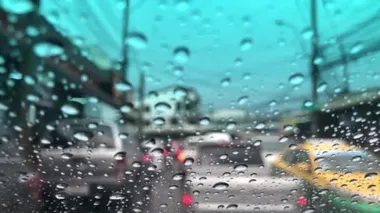 Araba ön camındaki yağmur damlasının odaklanmış görüntüsü, şehirdeki trafiği bulanıklaştırması, yağmur fırtınasında araba sürmesi, sokak lambasının renkli bokeh 'i, seçici odak noktası.